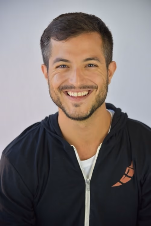 Smiling man with short dark hair and beard wearing a black zip-up hoodie and white shirt.