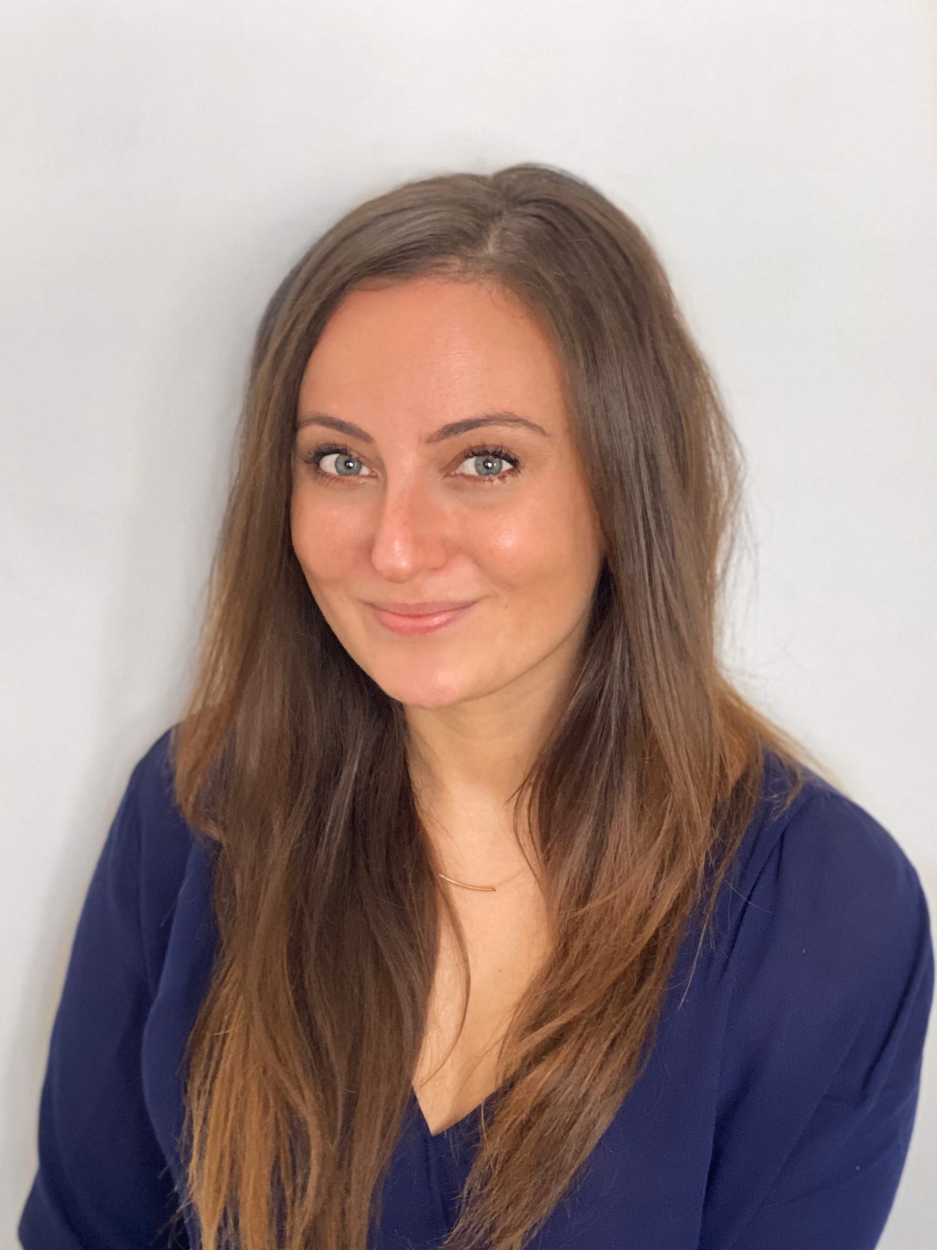 Smiling woman with long brown hair wearing a dark blue top against a plain white background.