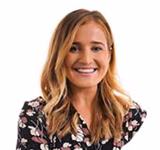 Smiling woman with long blonde hair wearing a black floral blouse on a white background.