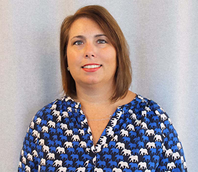 Woman with shoulder-length brown hair wearing a blue shirt patterned with white and black elephants.