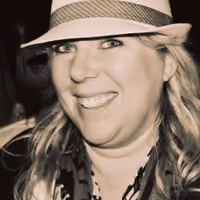 Smiling woman with long hair wearing a striped hat and patterned scarf in a close-up photo.