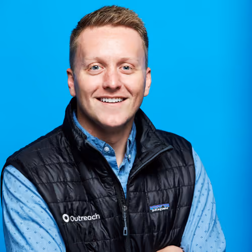 Smiling man wearing Outreach vest over a blue shirt against a plain blue background.