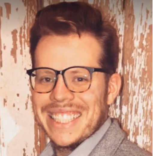 Smiling man with glasses, short brown hair, and a light beard wearing a gray jacket.
