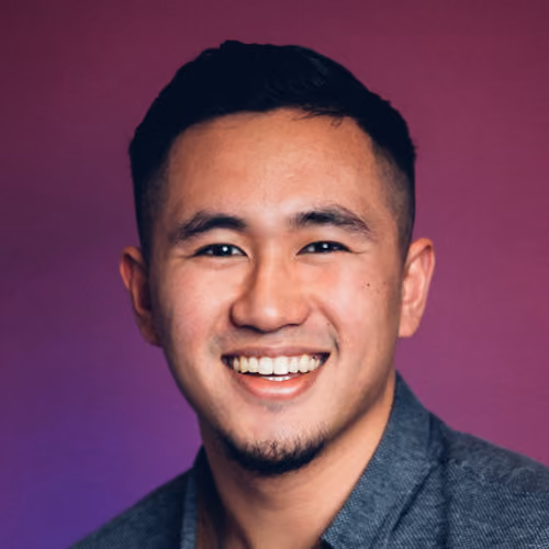 Young man with short black hair smiling in front of a purple gradient background.