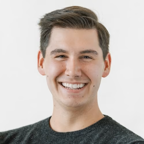 Smiling young man with brown hair wearing a dark gray sweater against a light background.