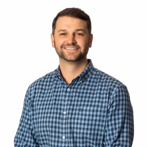 Smiling man wearing blue checkered shirt against white background.