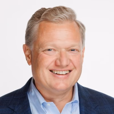 Smiling middle-aged man with light hair wearing a blue suit jacket and light blue shirt.