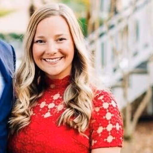 Smiling woman with long blonde hair wearing a red lace dress standing outdoors.
