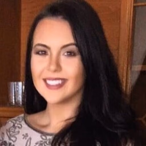 Young woman with long dark hair smiling indoors against wooden background.