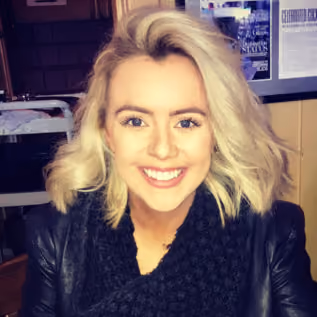 Smiling woman with blonde hair wearing a black scarf and leather jacket in indoor setting.