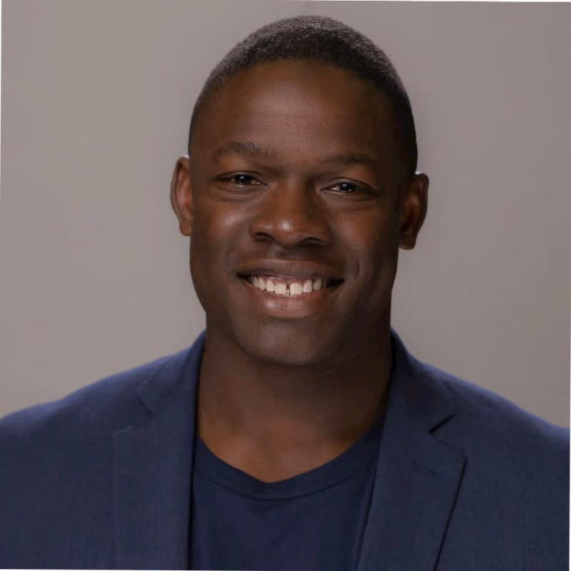 Close-up of a smiling man wearing a navy blue blazer and shirt against a plain background.