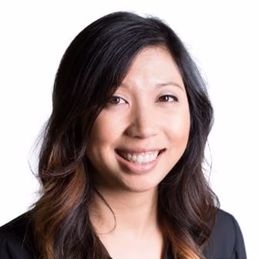 Smiling woman with long dark hair wearing a black top against a white background.