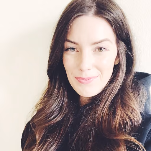 Woman with long brown hair smiling softly against a plain light background.