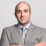 Man in gray suit and patterned tie with arms crossed against a light background.