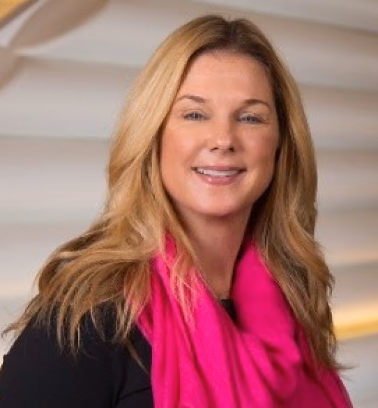 Smiling woman with long blonde hair wearing a bright pink scarf and a black top.