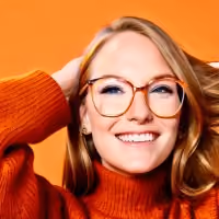 Smiling woman with glasses wearing an orange sweater against an orange background.