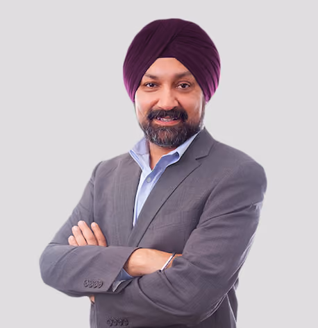 Man wearing a purple turban and gray suit with folded arms, smiling at the camera.