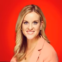 Smiling woman with blonde hair wearing a peach blazer against a red background.