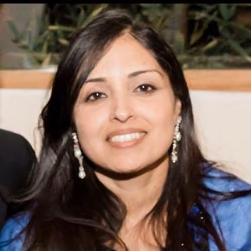 Smiling woman with long dark hair wearing pearl drop earrings and a blue top.