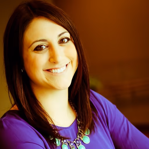 Smiling woman with long dark hair wearing a purple top and green statement necklace.