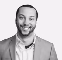 Smiling man with short hair wearing a light jacket and shirt, facing forward on a white background.