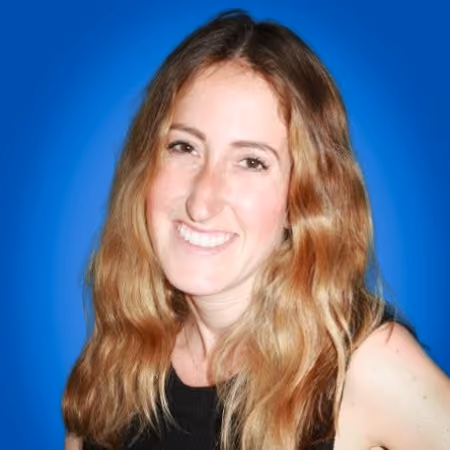Smiling woman with long wavy blonde hair wearing a black sleeveless top against blue background.