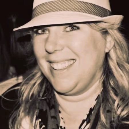Smiling woman wearing a light hat and patterned scarf in a close-up portrait.