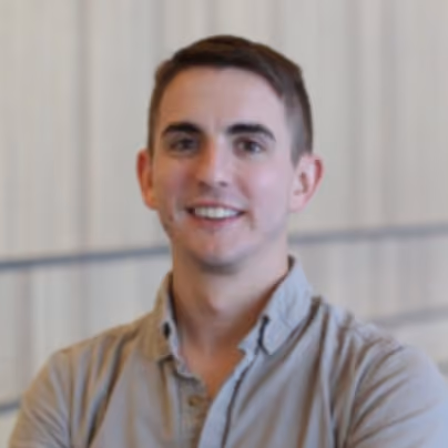 Smiling young man with short brown hair wearing a beige button-up shirt posed indoors.
