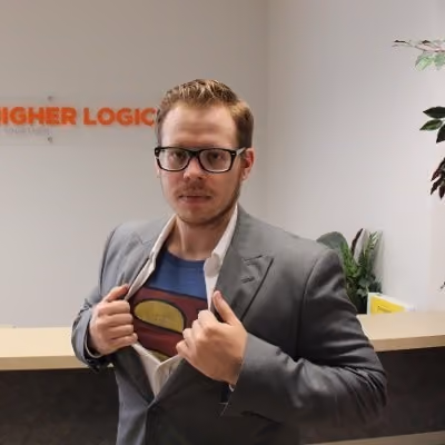 Man in glasses and suit opening shirt to show Superman logo underneath in an office setting.