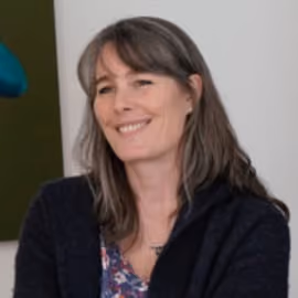 Smiling woman with shoulder-length brown hair wearing a dark sweater and floral blouse.