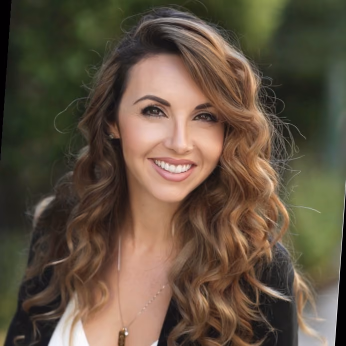 Smiling woman with long curly hair wearing black blazer and white top outdoors.