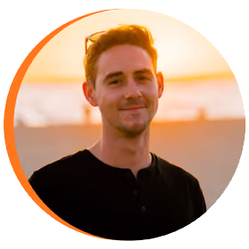Young man with short brown hair wearing a black shirt standing outdoors at sunset.