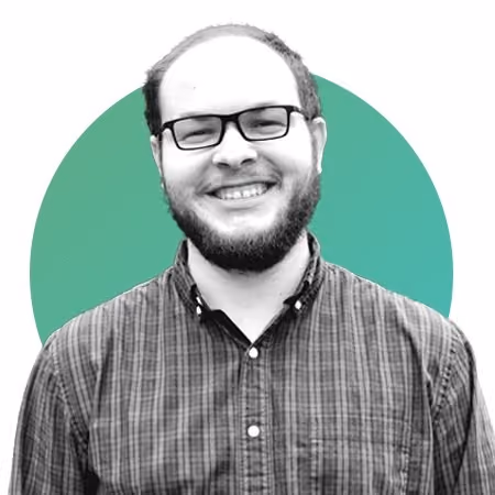 Smiling man with glasses and beard wearing a checkered shirt in front of a teal circle background.