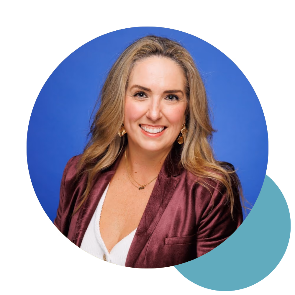 Smiling woman with long blonde hair wearing a burgundy jacket and white top on blue background.