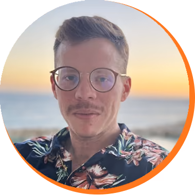 Man with glasses and short hair wearing a floral shirt with a beach sunset background.