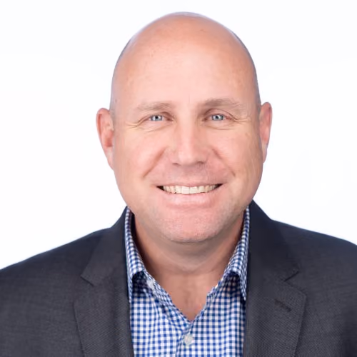 Smiling bald man in a dark blazer and checkered blue shirt on a white background.