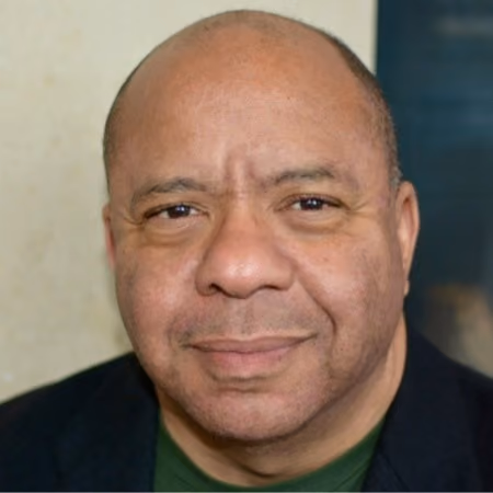 Close-up portrait of a middle-aged man with a calm expression, wearing a dark jacket and green shirt.