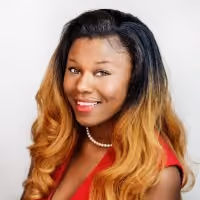 Smiling woman with long ombré hair wearing a red top and pearl necklace against white background.