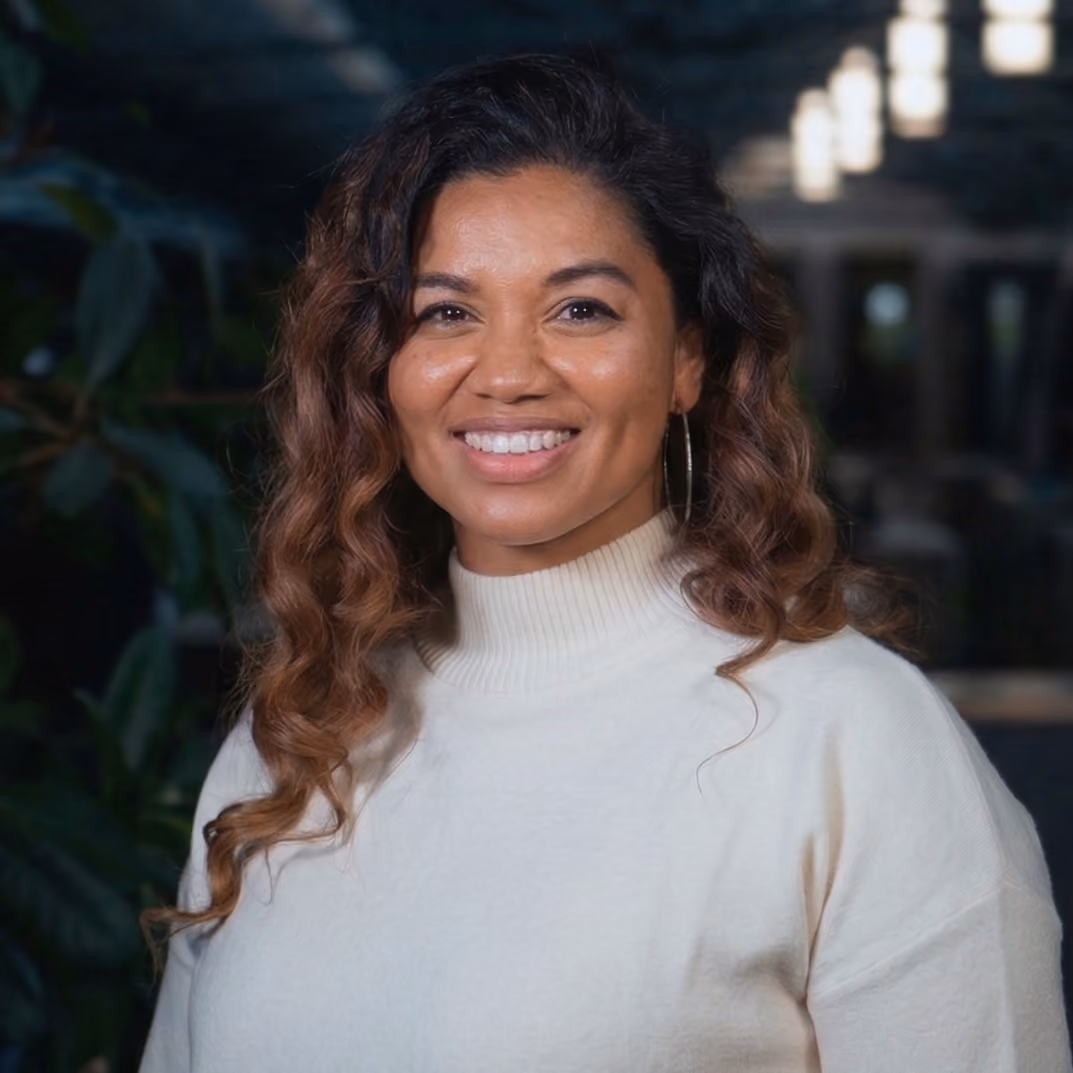Smiling woman with curly hair wearing a white turtleneck sweater and hoop earrings indoors.