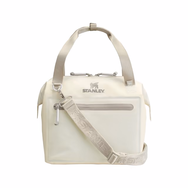 Cream-colored Stanley soft cooler bag with beige handles, front zippered pocket, and adjustable shoulder strap branded with Stanley logo.