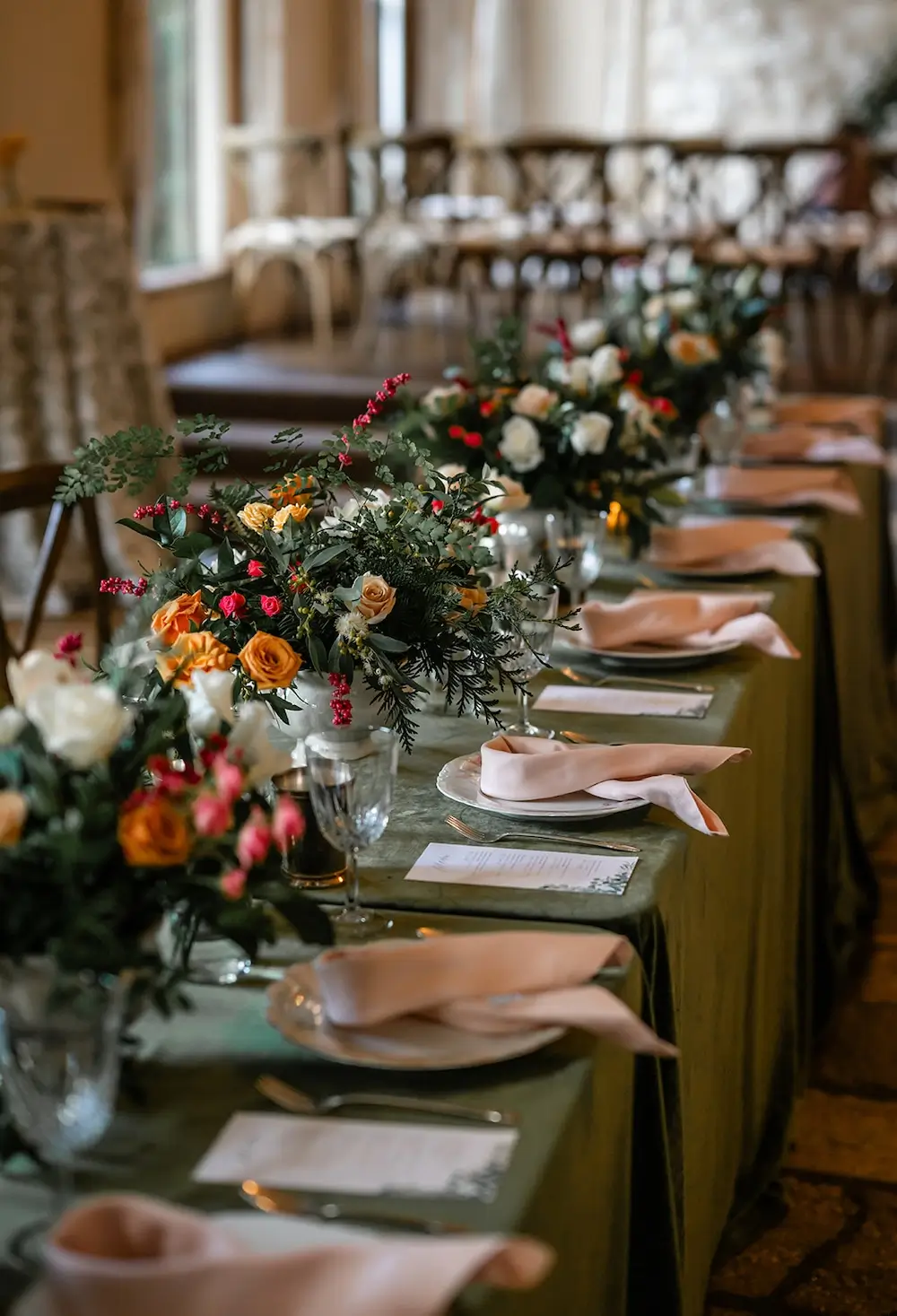Intimate micro wedding reception table with lush floral centerpieces in coral, orange, and white, paired with soft pink napkins and greenery accents.