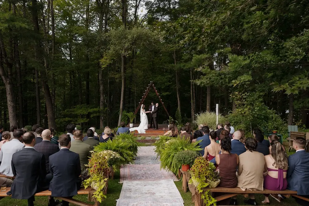 outdoor micro wedding ceremony in forest setting with couple exchanging vows and guests seated on benches