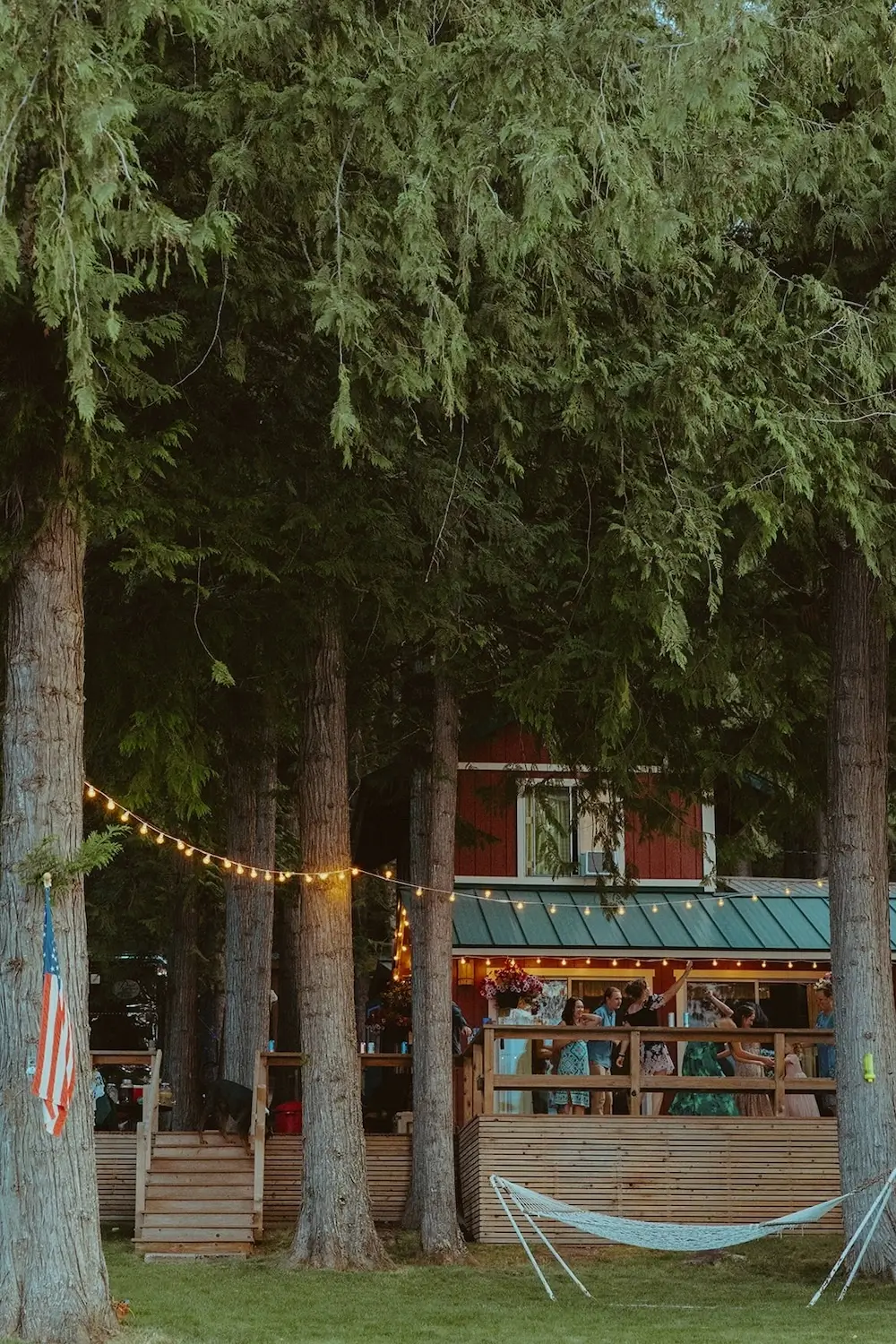 Woodland lakeside micro wedding reception at a cozy cabin with string lights and guests celebrating on a deck surrounded by trees.