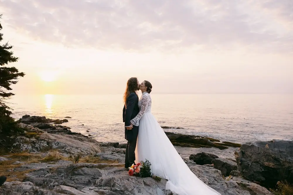 Couple overlooking a mountain lake at sunrise during an intimate Acadia National Park wedding, with the bride’s gown flowing over rocky cliffs in the early morning light.