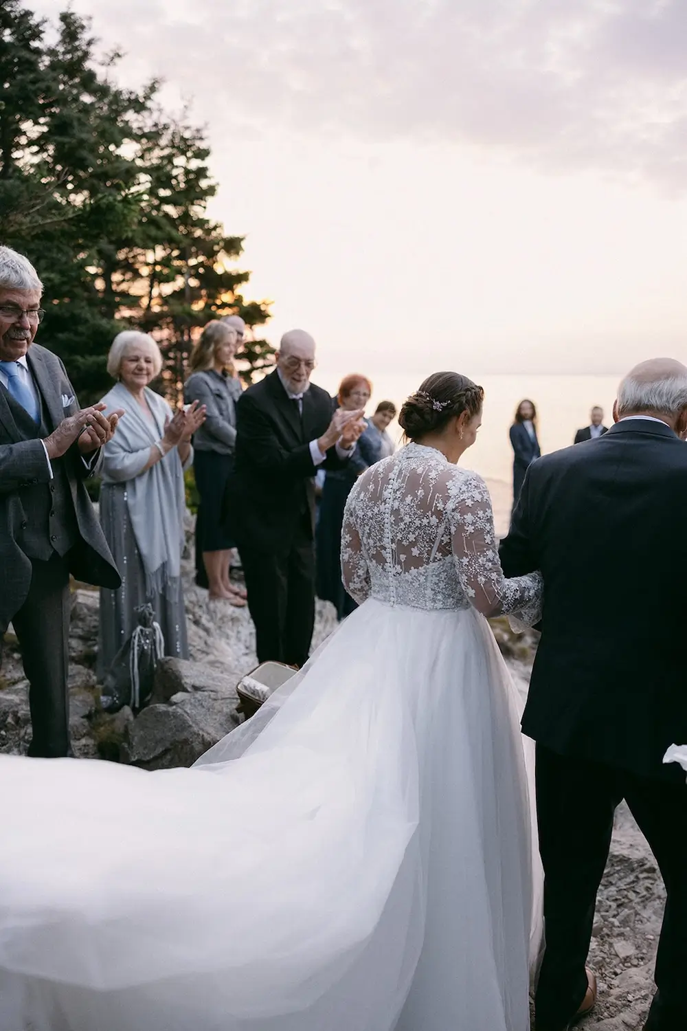 Bride walking down a rocky aisle with her father as guests stand and watch.