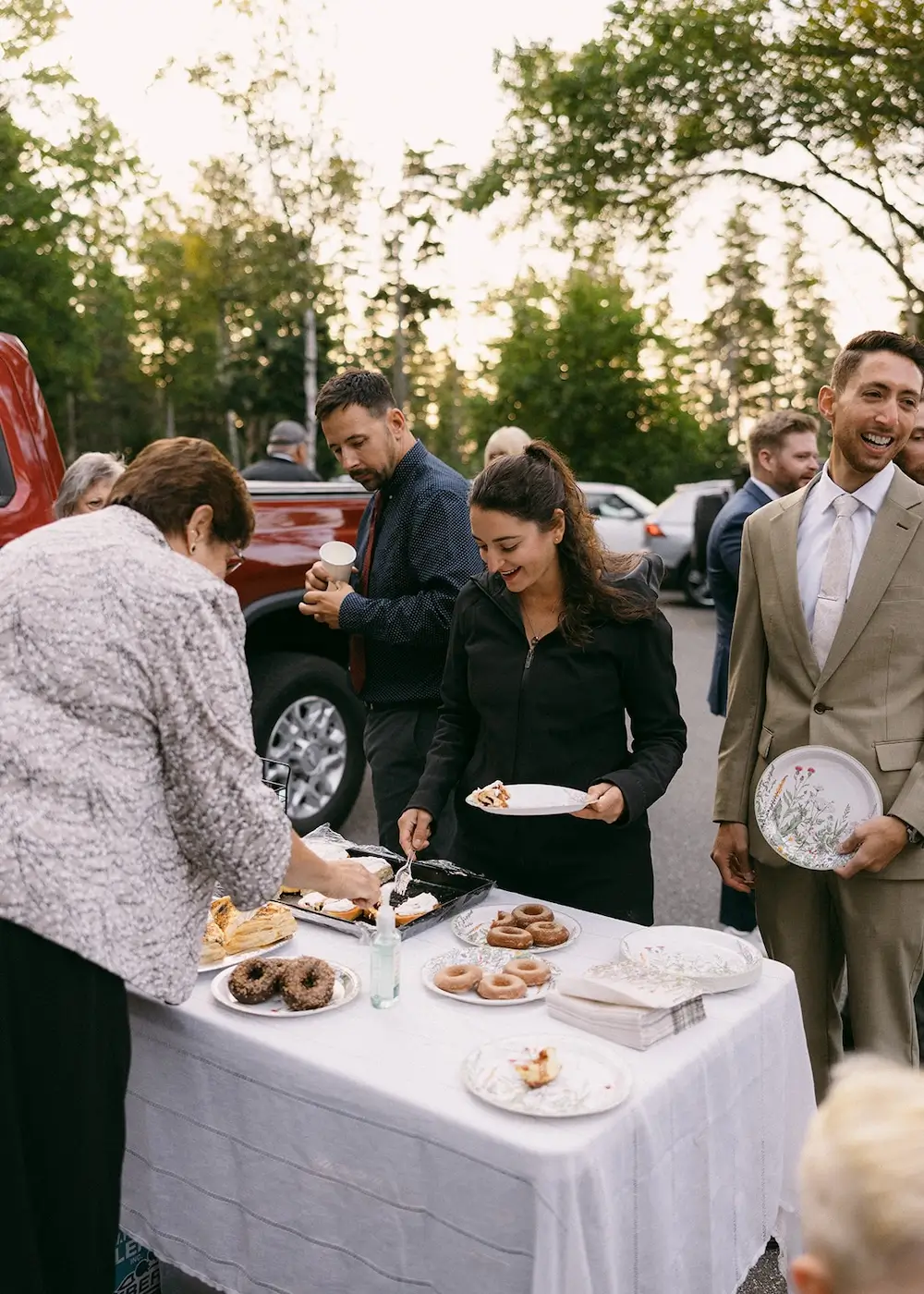 Guests serving themselves coffee and pastries from a table at an outdoor wedding.