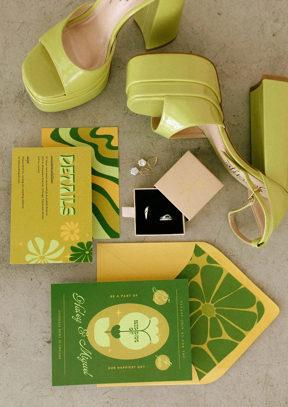 Flat lay of mid-century modern wedding details featuring lime-green platform heels, retro-inspired green and yellow invitations, wedding rings, and pearl earrings.