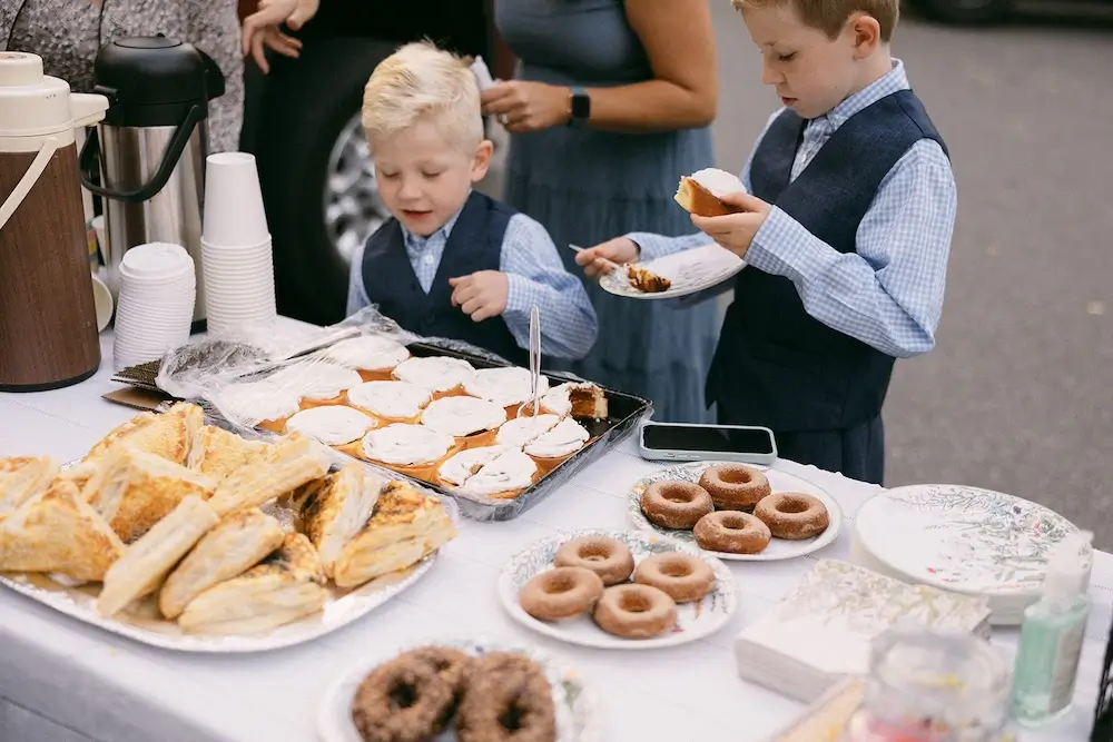 Children picking pastries and donuts from a dessert table during a casual wedding brunch cocktail hour.