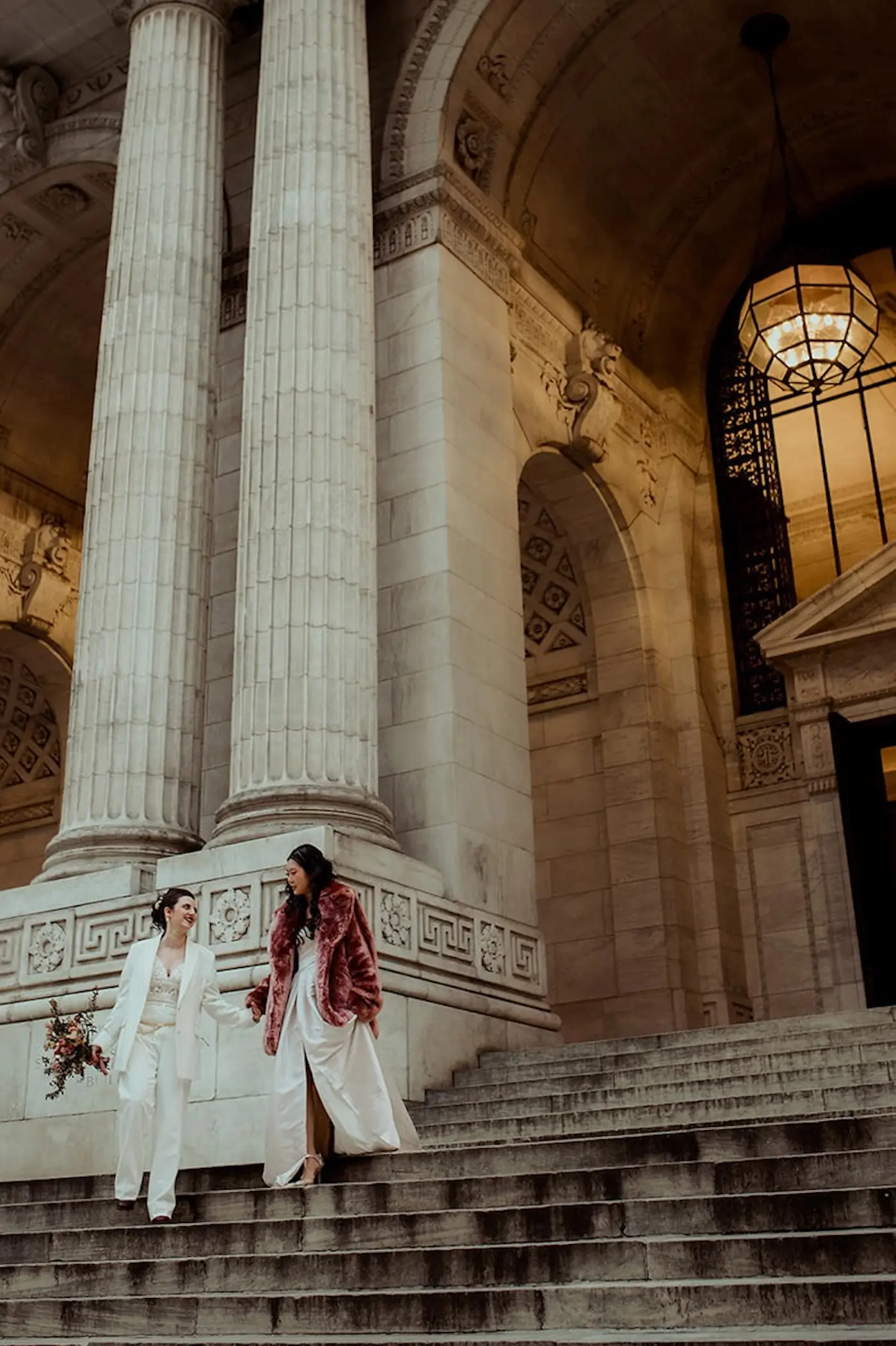 Couple walking down grand courthouse steps between tall stone columns.