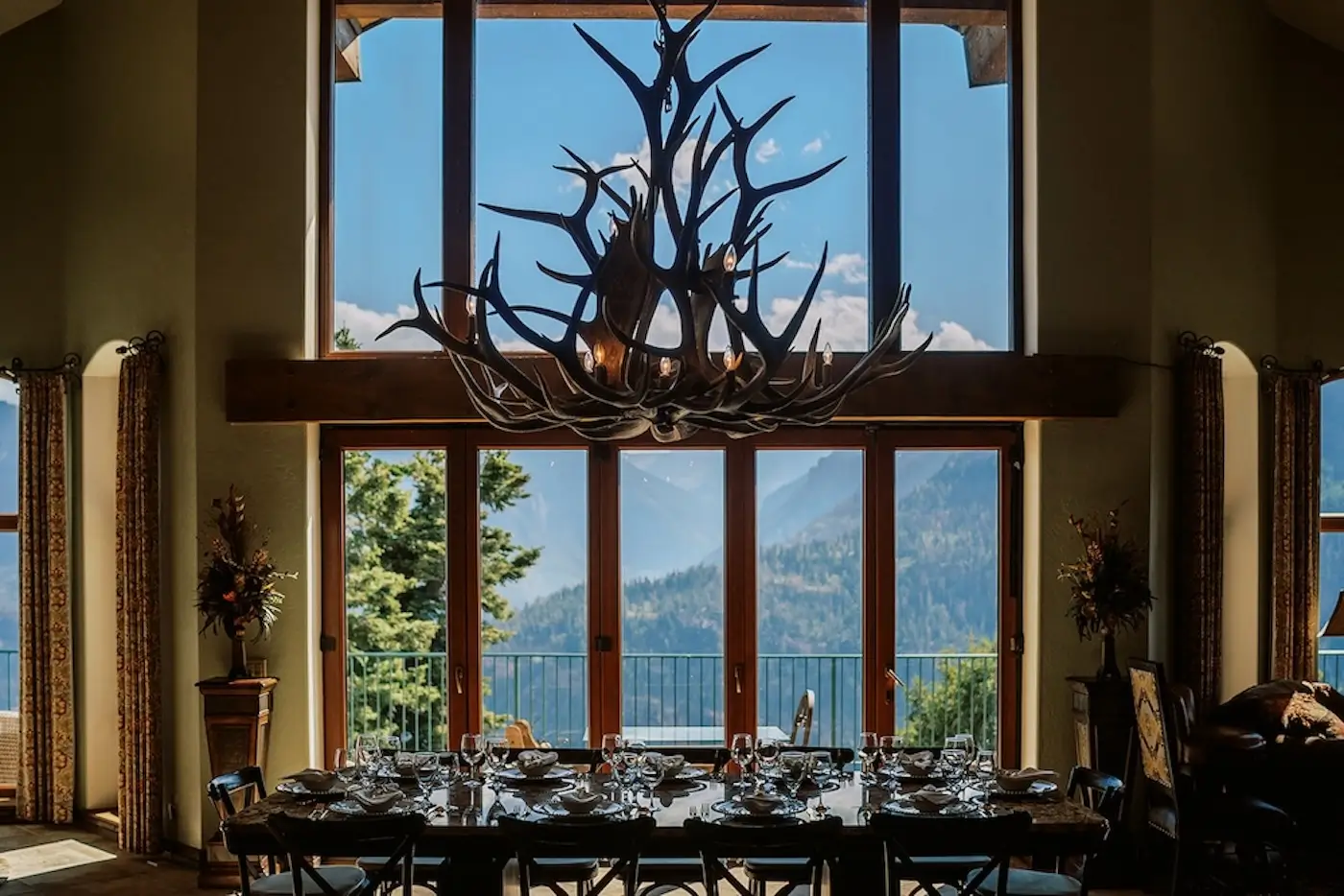 Mountain lodge reception table beneath large antler chandelier with scenic mountain views.